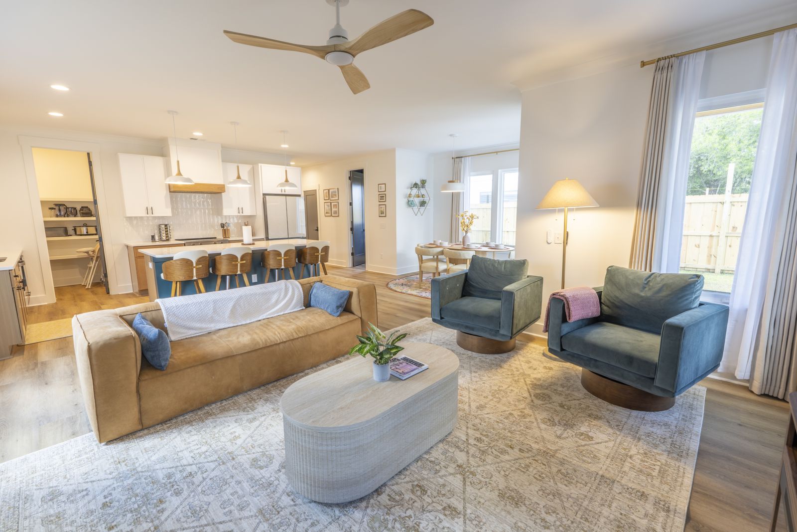 Living room with a cognac leather sofa and two blue swivel chairs, the kitchen and dining area beyond