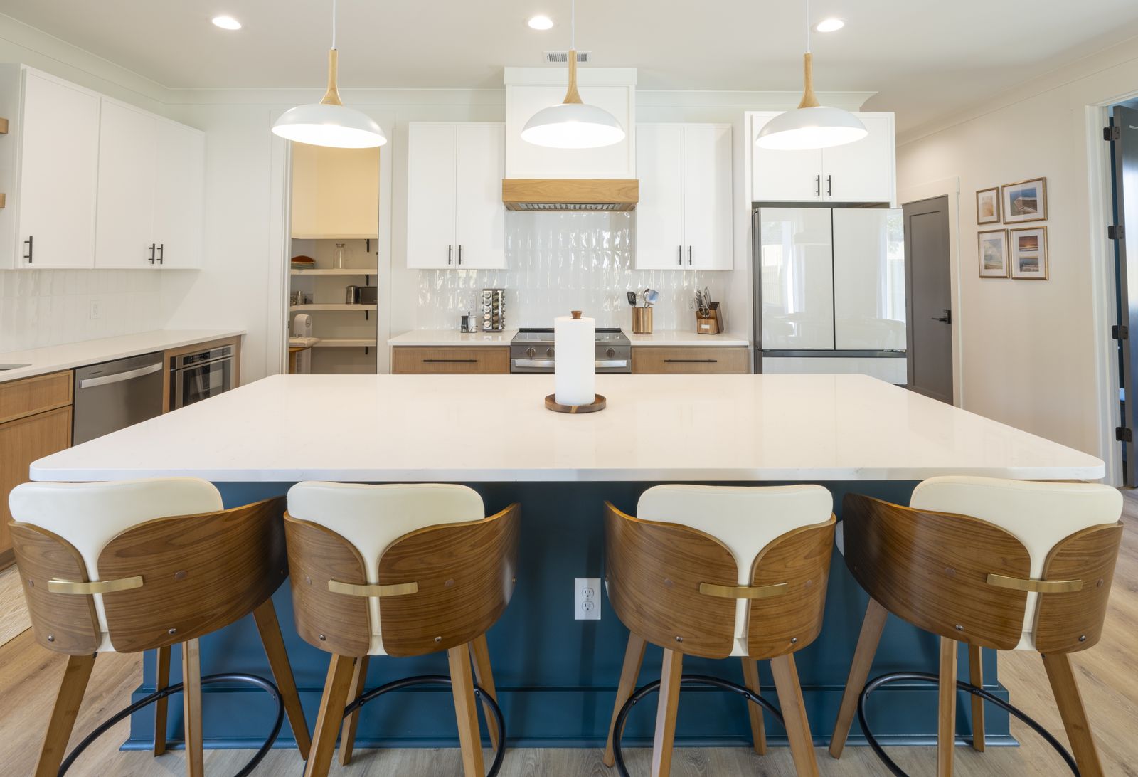 Kitchen island with four wood and cream counter stools under pendant lights, white cabinetry beyond