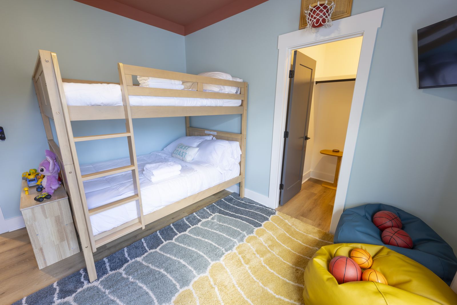 Kids' bunk room with a light wood bunk bed, beanbags, a mini hoop over the door, and a coral ceiling