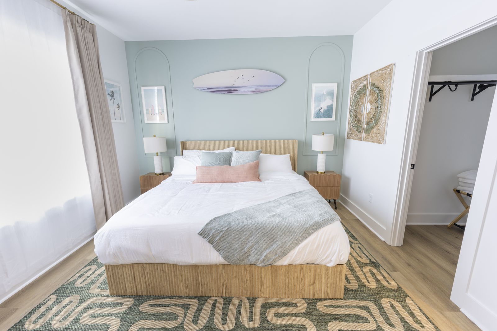 Coastal bedroom with a rattan headboard, a surfboard on the wall, and a patterned rug