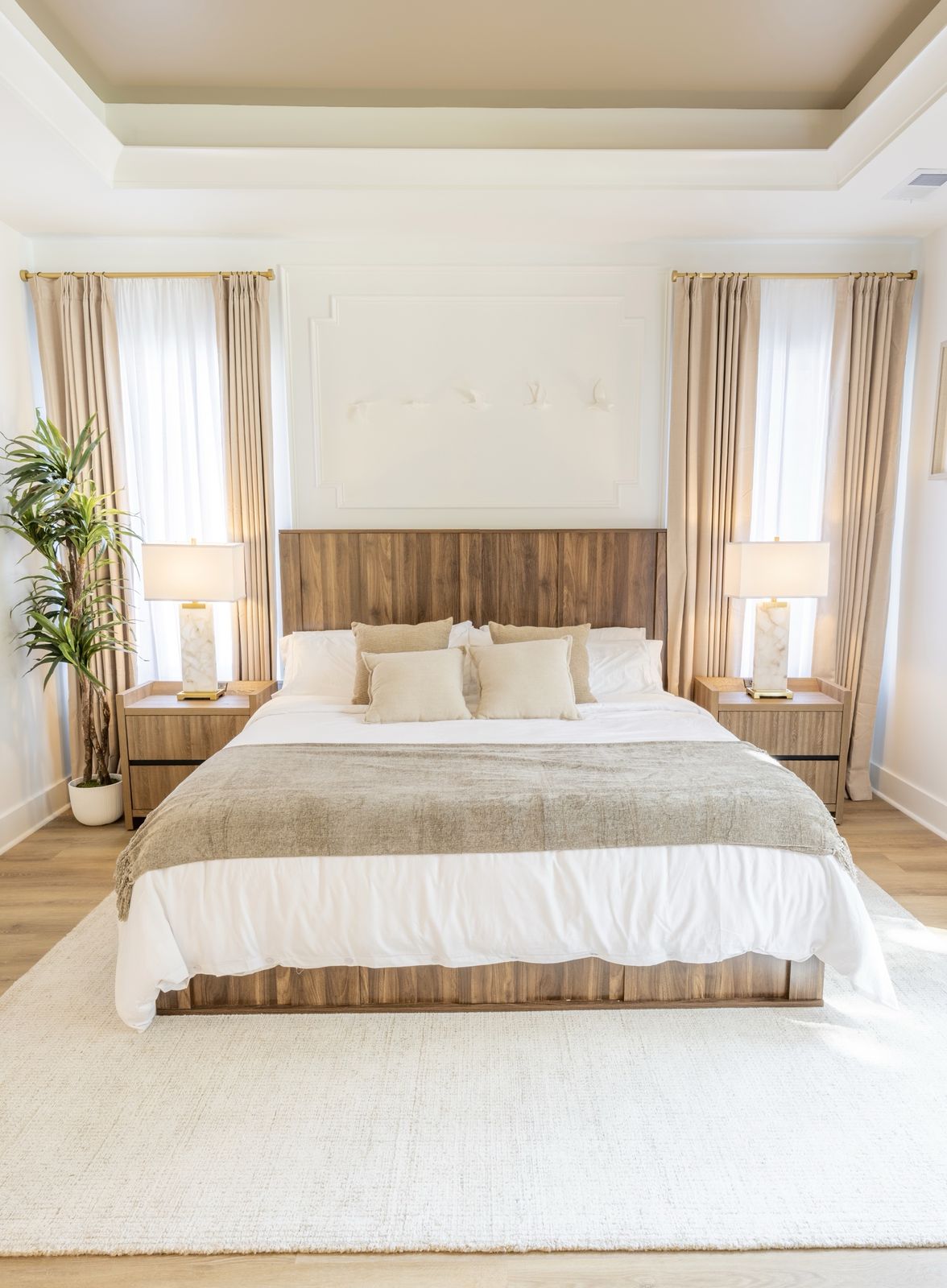 Primary bedroom with a tray ceiling, wood headboard, matching alabaster lamps, and neutral bedding