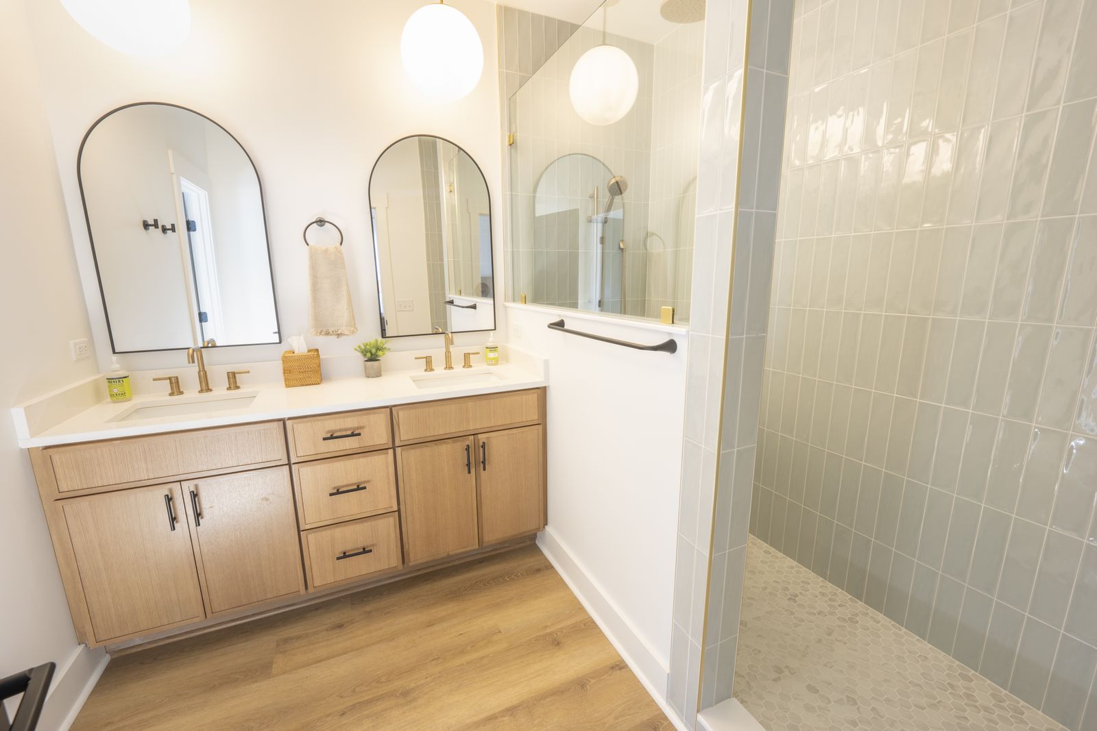 Primary bath with two arched mirrors over a wood double vanity and a sea green tiled walk in shower