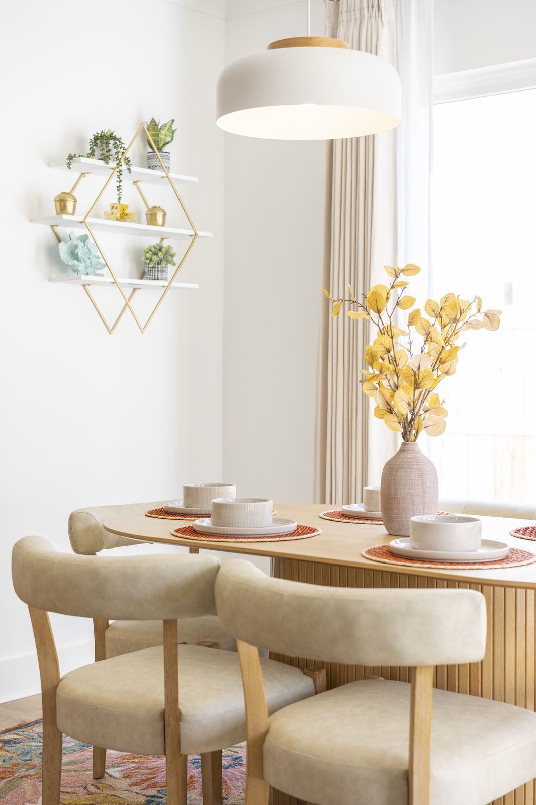 Dining table set with stoneware and woven placemats under a white pendant light, golden branches in a vase